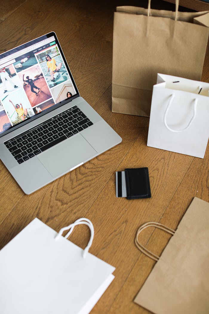 Laptop with shopping bags and a credit card on a wooden floor, symbolizing online shopping.